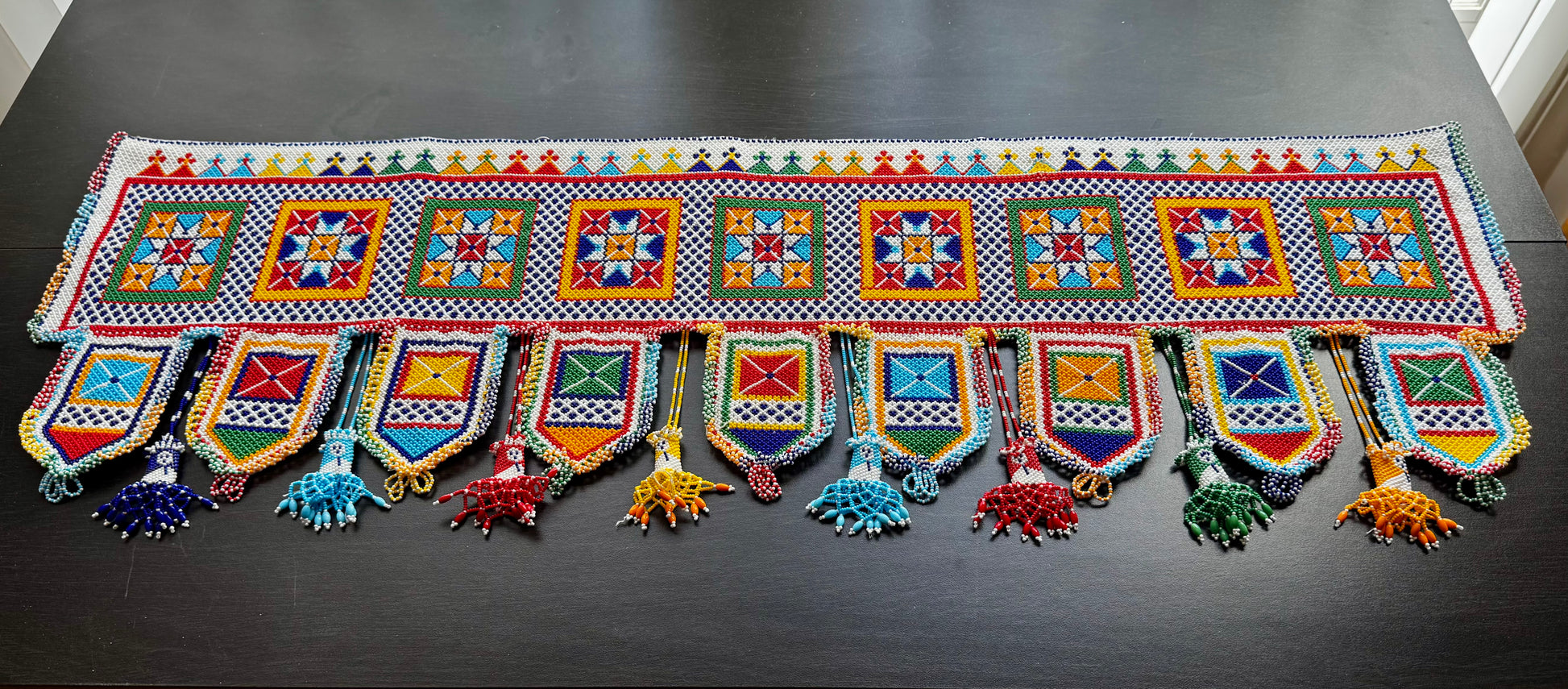 Colorful decorative Motikaam valance with patterns and tassels on a dark surface