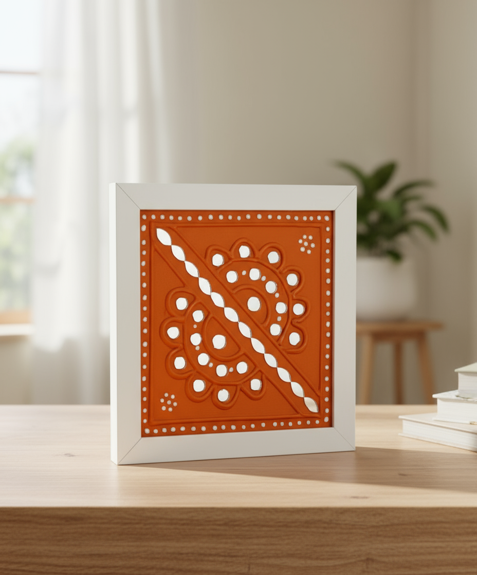 Decorative framed artwork with a geometric pattern on an orange background, placed on a wooden surface.