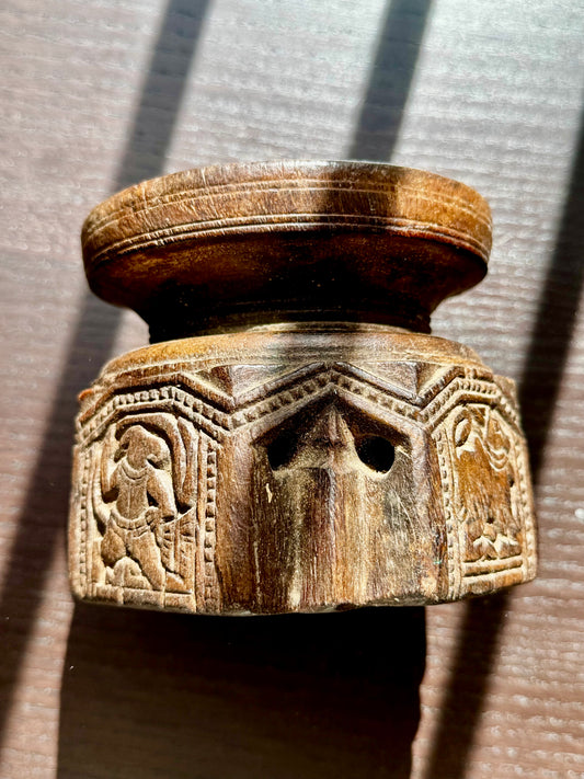 Wooden candle holder on its side with intricate carvings on a textured surface