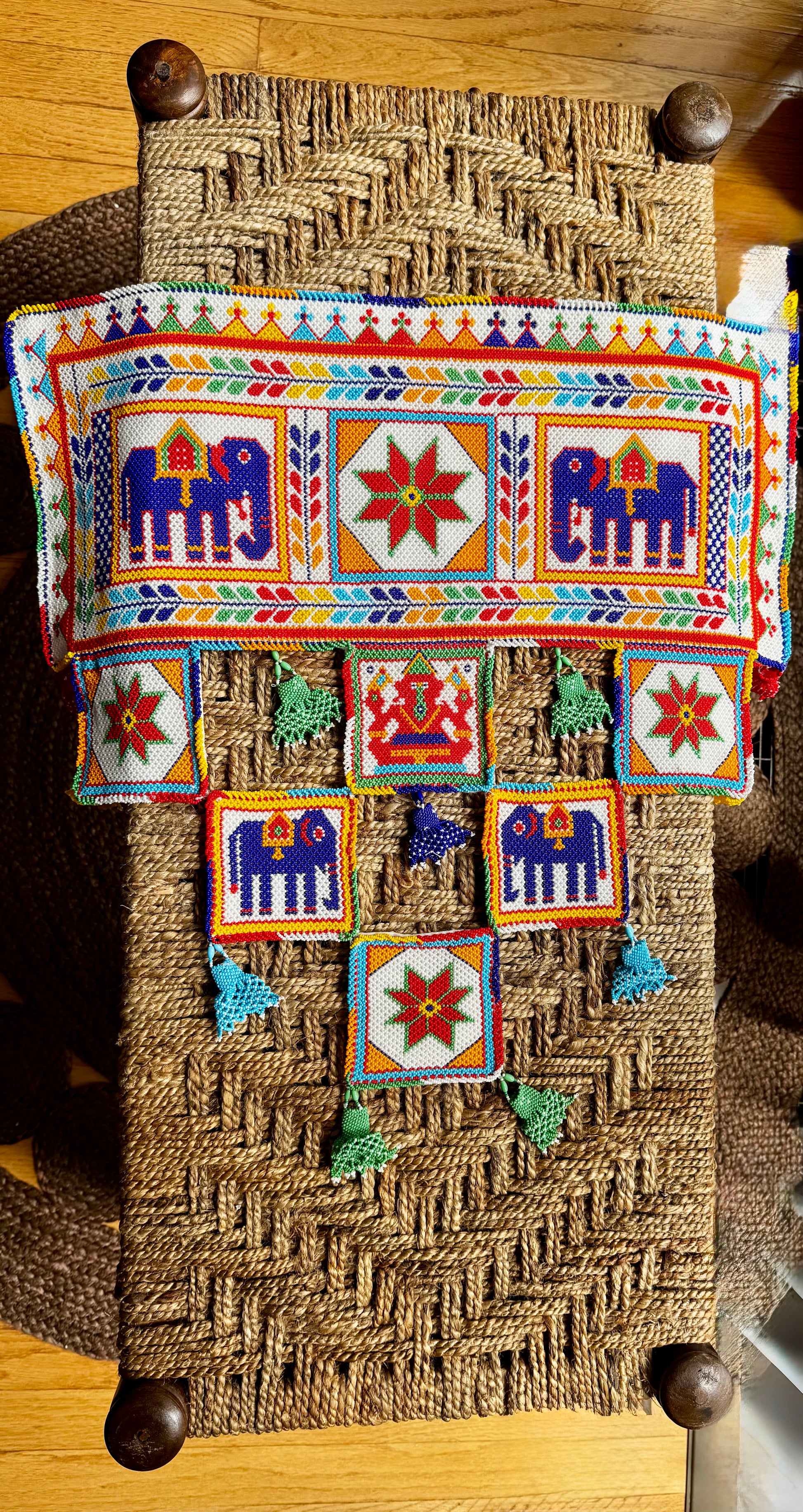 Decorative Motikaam - strung Pearl work Ganesha wall hanging with colorful design on a textured fabric background Decorative wall hanging with colorful patterns on a woven surface