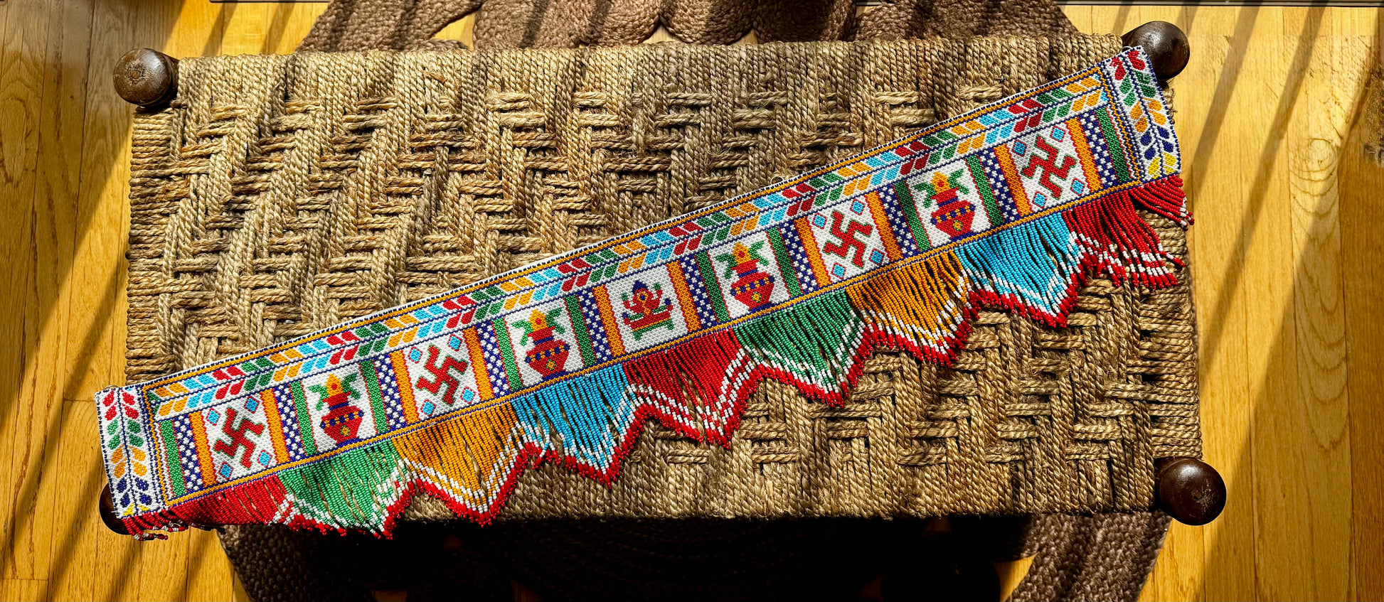Decorative Motikaam - strung Pearl work wall hanging with colorful design on a textured fabric background Colorful decorative border with patterns on a woven surface