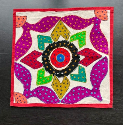 Colorful embroidered fabric square with a geometric pattern on a dark background