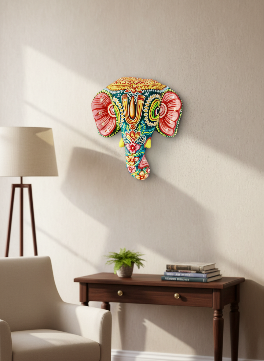 Decorative wall art of an elephant head on a plain wall with a lamp and table in the background.