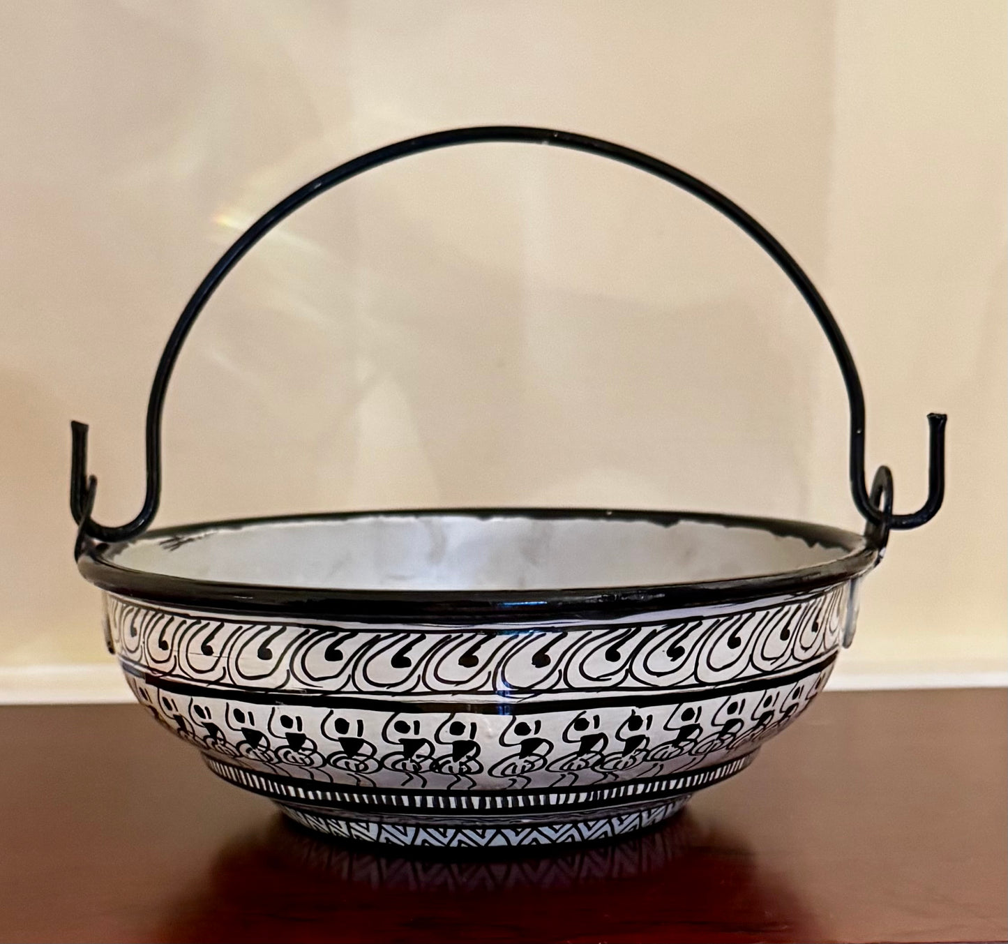 Decorative black and white patterned bowl with a handle on a wooden surface.