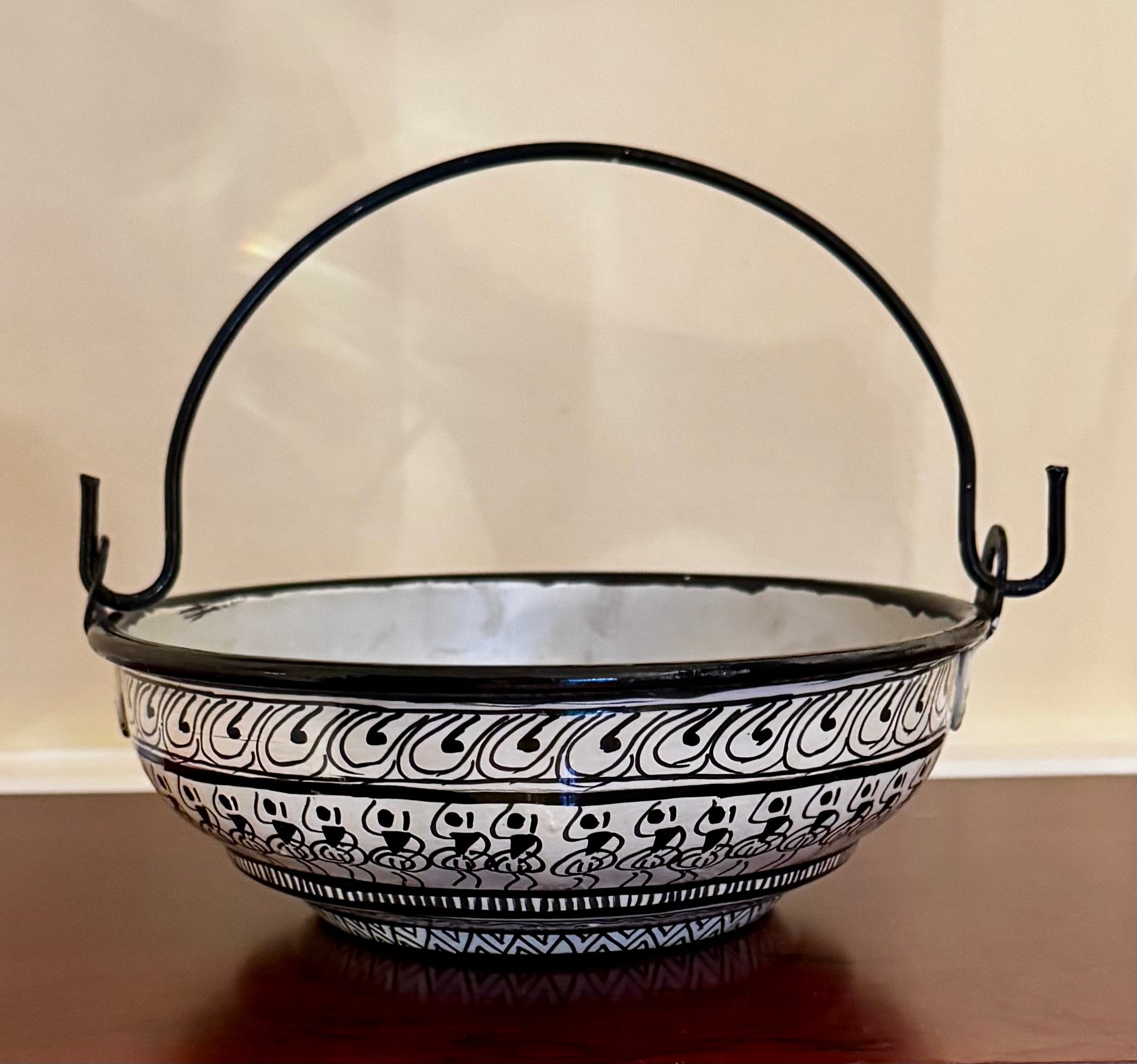 Decorative black and white patterned bowl with a handle on a wooden surface.
