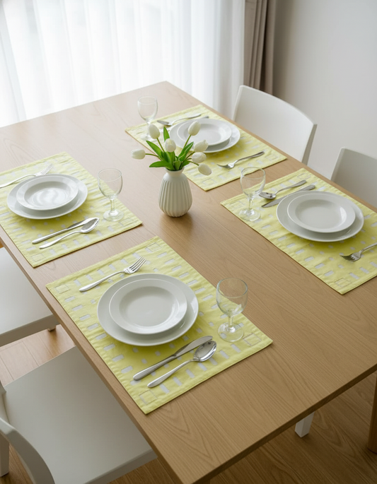 Dining table set with plates, cutlery, and a vase of flowers on yellow placemats.