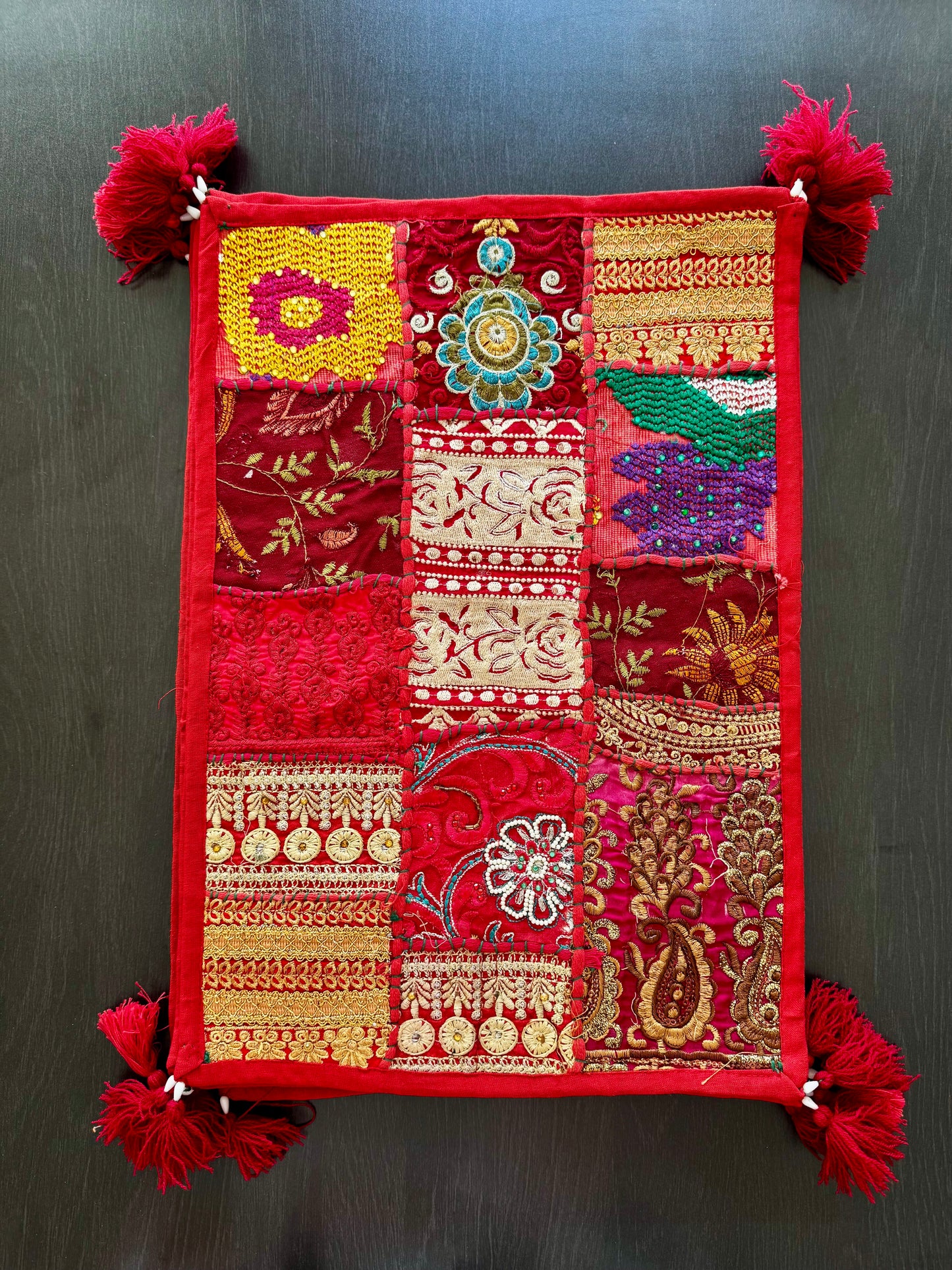 Decorative red Khambhadia patchwork placemats with intricate patterns and tassels on a dark background