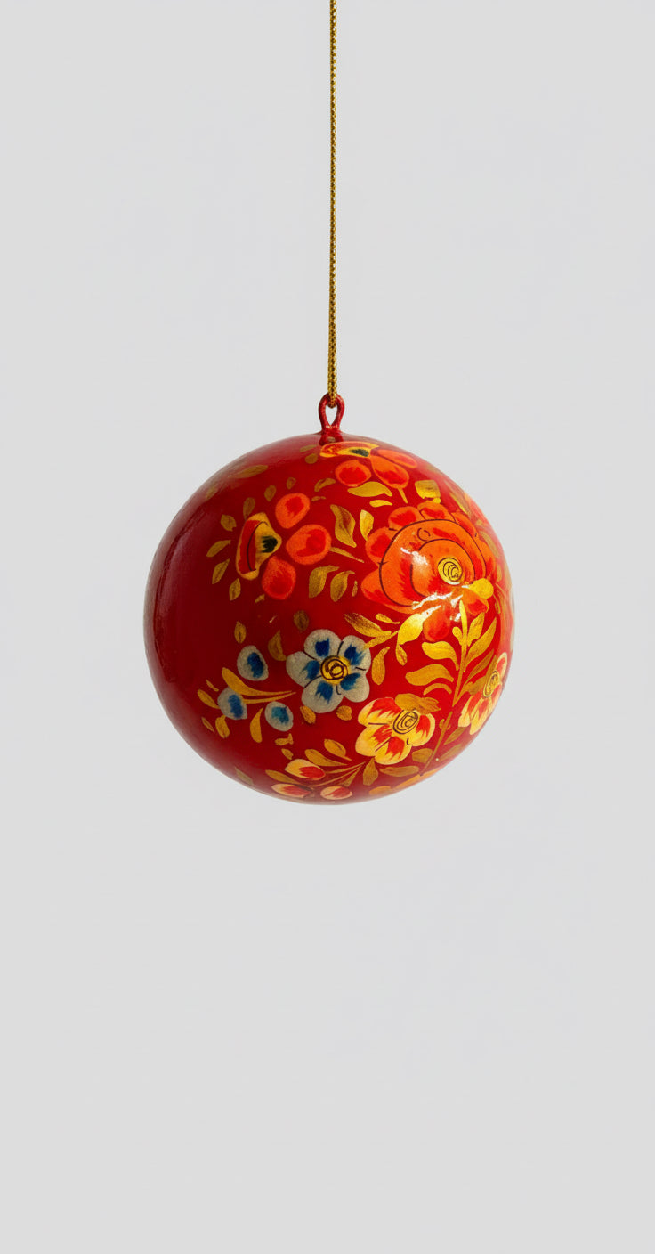 Red decorative ball with floral patterns on a gold chain, held in front of a kitchen background.