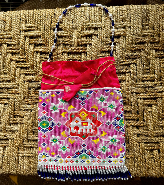 Colorful hand made pearl embroidered handbag/Batwa/Potlis with a pink top section on a woven surface