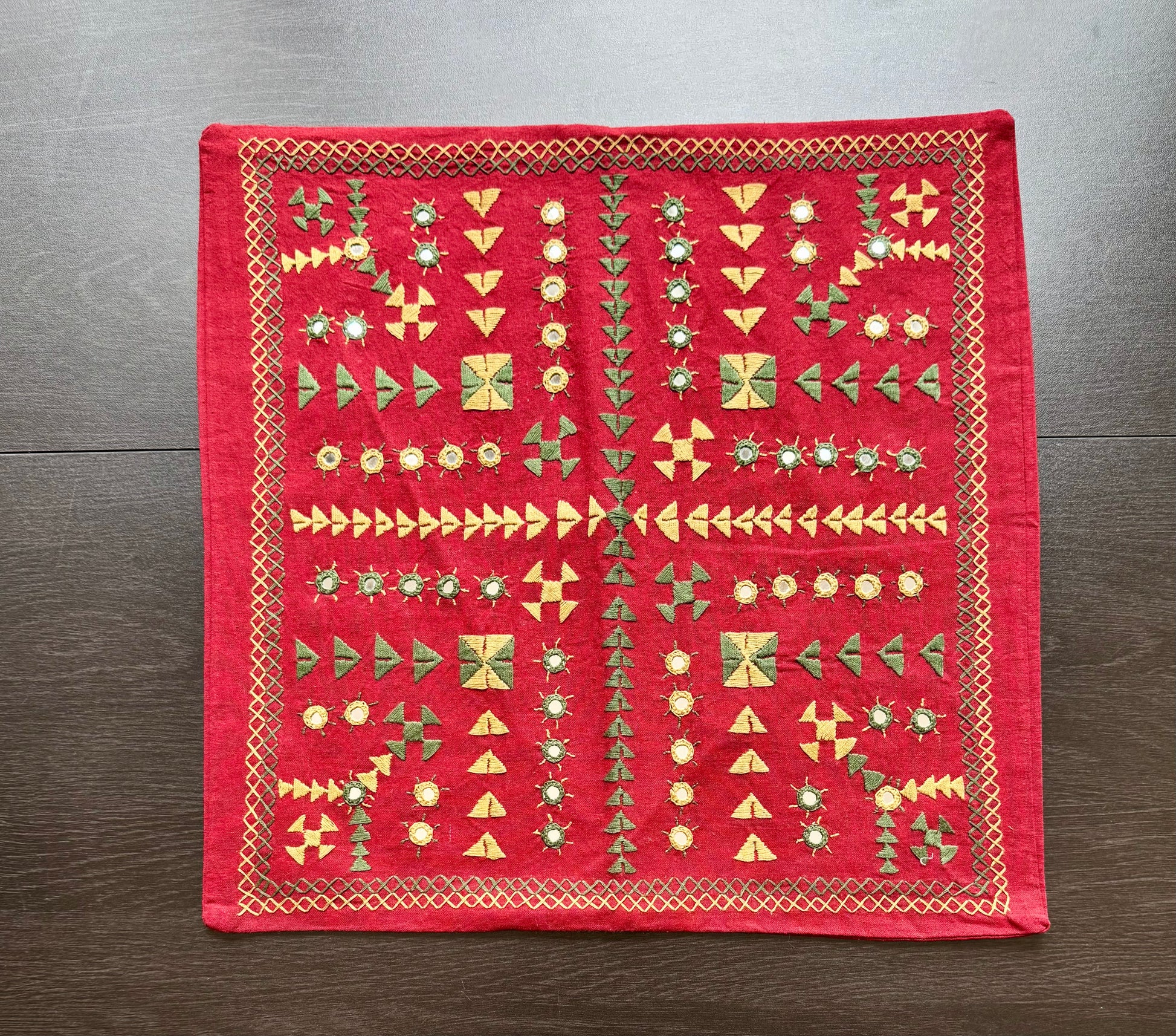 Red embroidered fabric cushion cover with geometric Kutchi embroidery patterns on a wooden surface