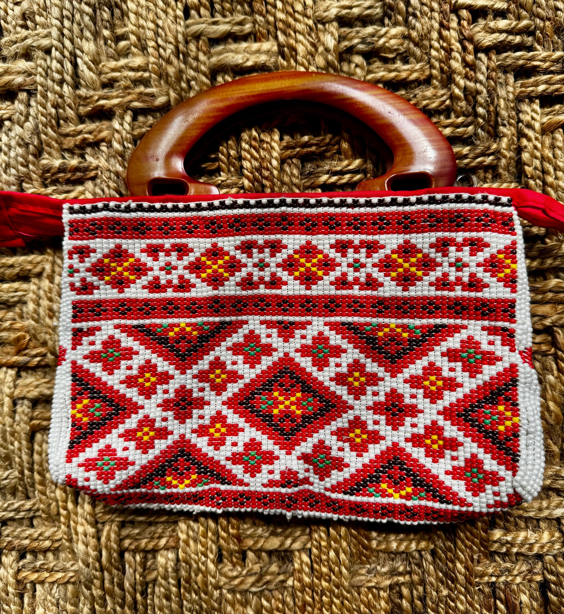 Decorative Motikaam - strung Pearl work Handbag with geometric pattern and wooden handle on a woven background