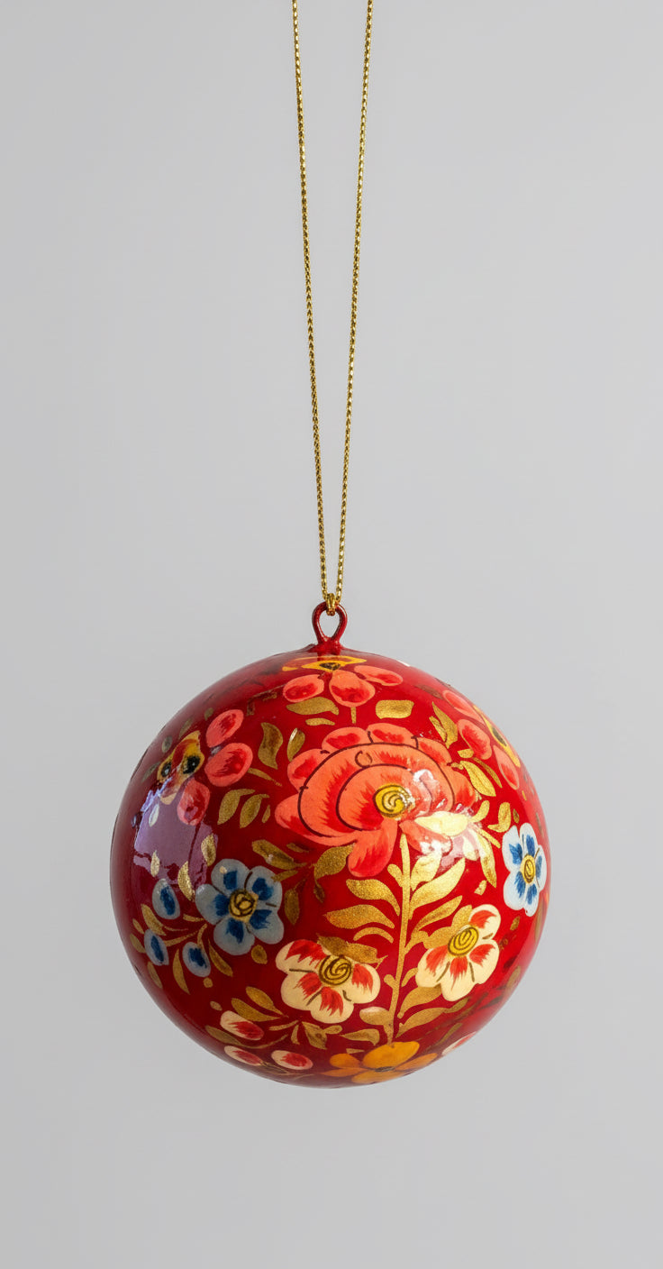 Decorative red ball with floral patterns hanging by a gold string against a neutral background.