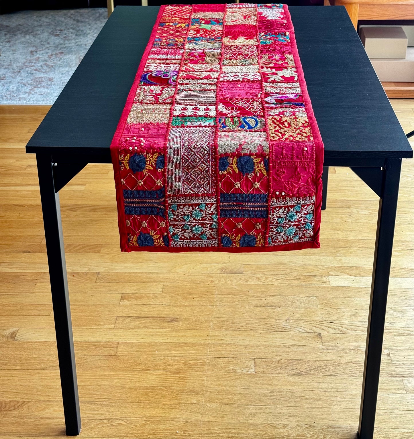Colorful Khambhadia patchwork table runner on a black table with a wooden floor background