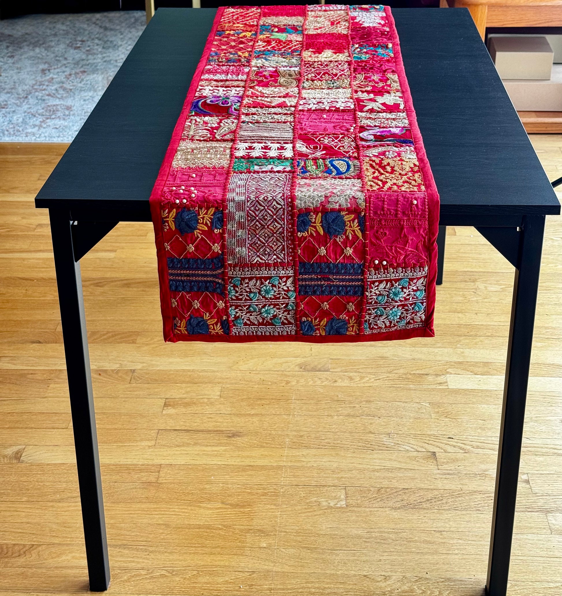 Colorful Khambhadia patchwork table runner on a black table with a wooden floor background