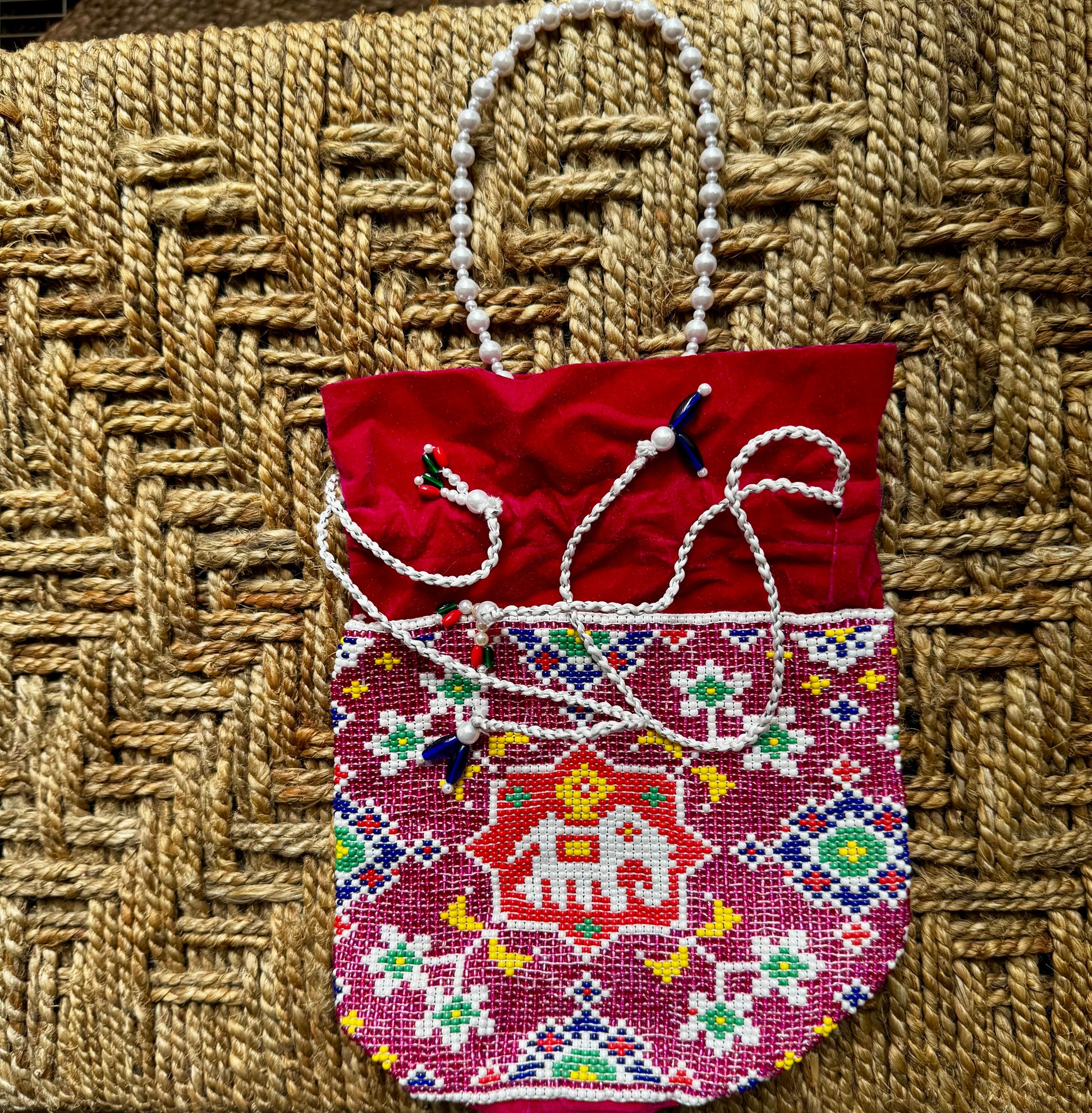 Decorative red bag/batwa/potli with intricate Pearl work on a textured woven surface