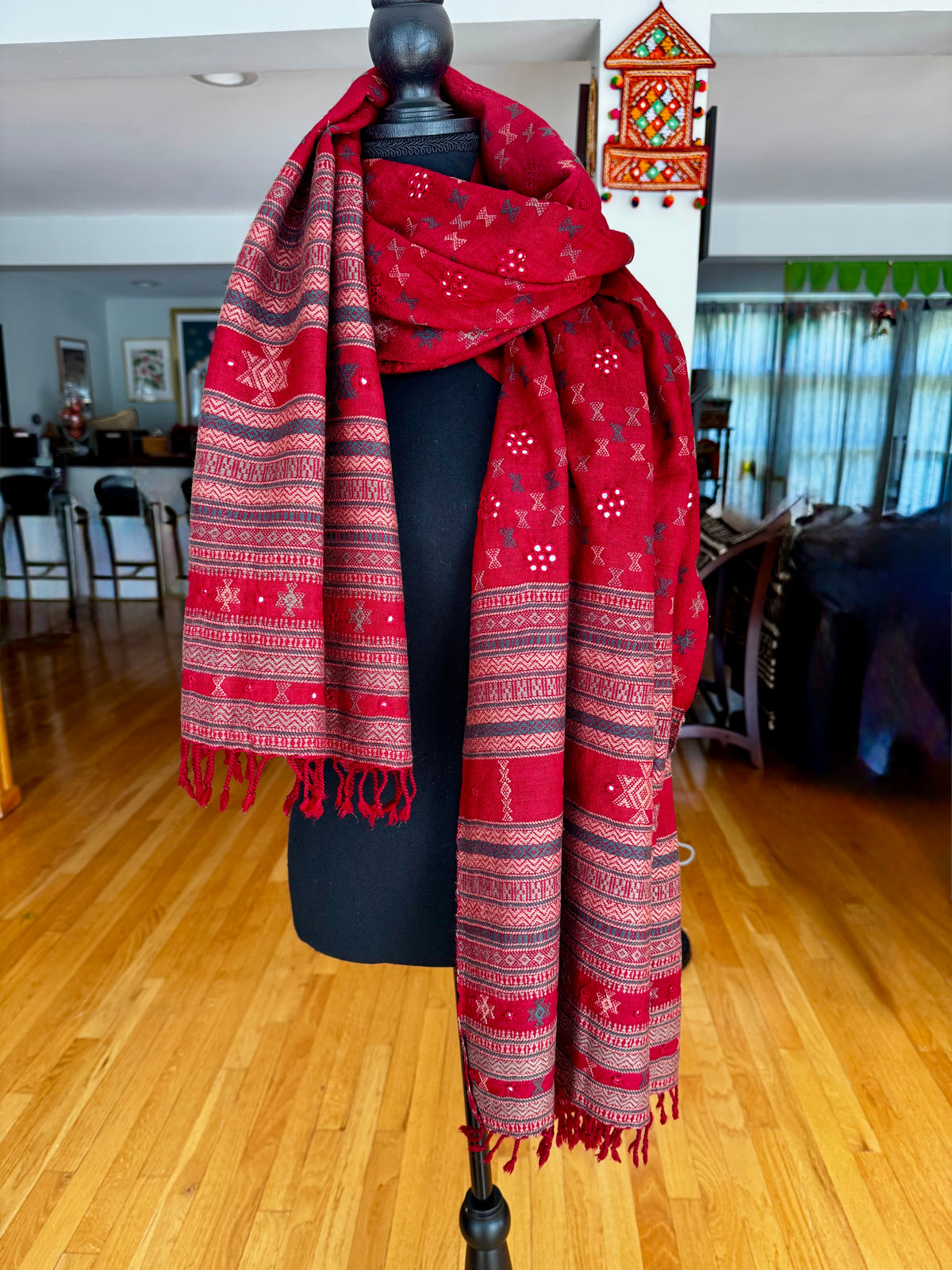 Red Kutchi Soof embroidered patterned scarf on a mannequin in a room with wooden floor and furniture.