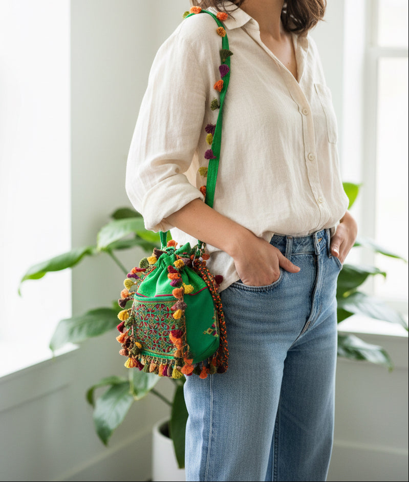 Person wearing a white shirt and blue jeans with a colorful green Soof embroidered Kutchi bag.
