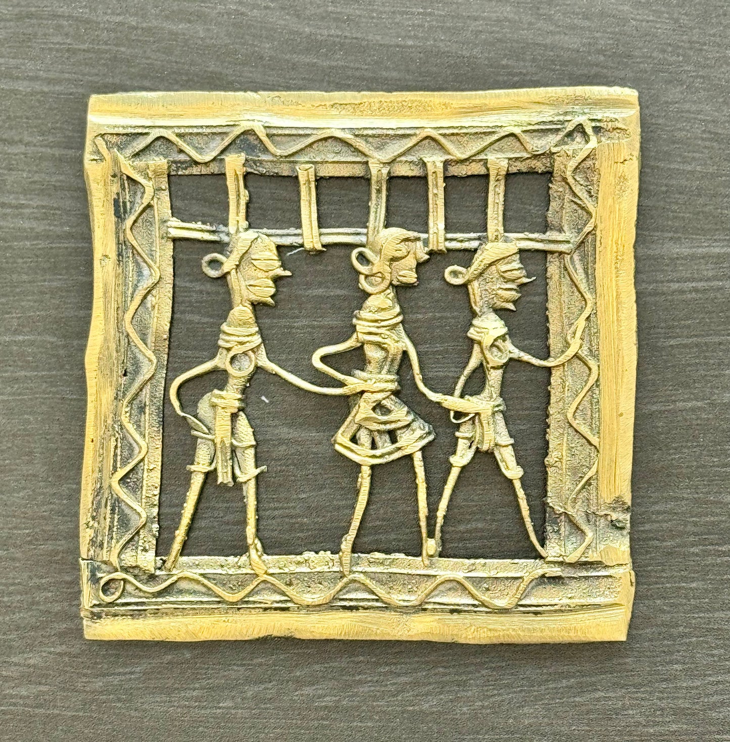Decorative brass Dhokra piece with three figures in a decorative frame on a wooden surface