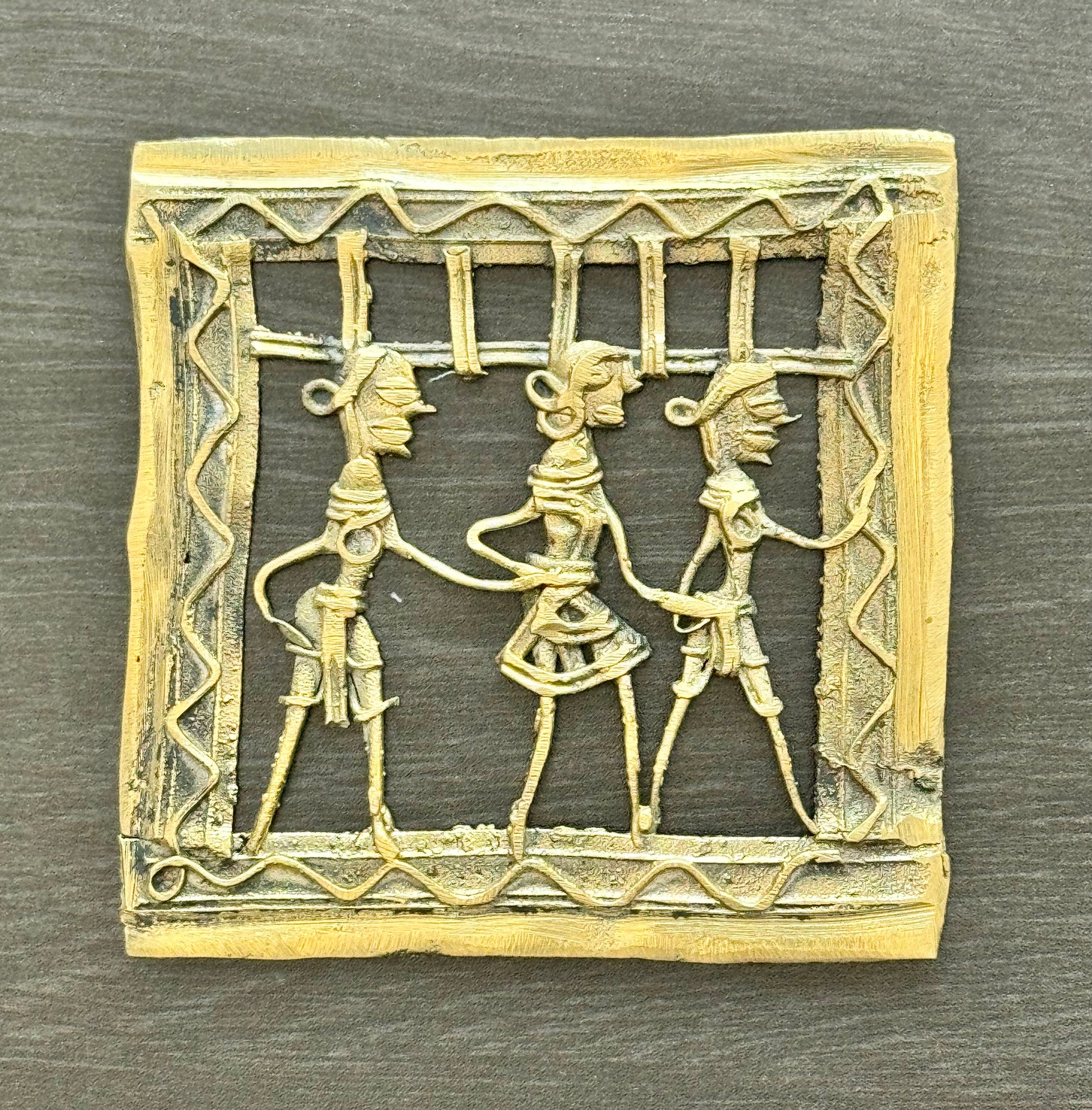Decorative brass Dhokra piece with three figures in a decorative frame on a wooden surface