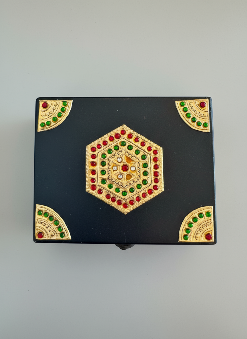 Decorative black box with gold and colored gemstone accents on a gray background