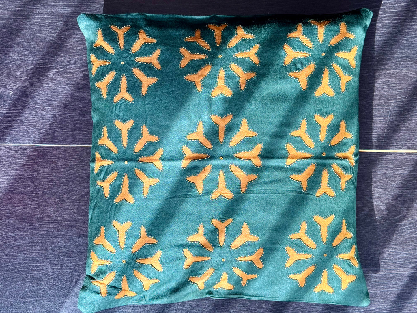 Teal pillow with yellow geometric pattern on a dark purple fabric background