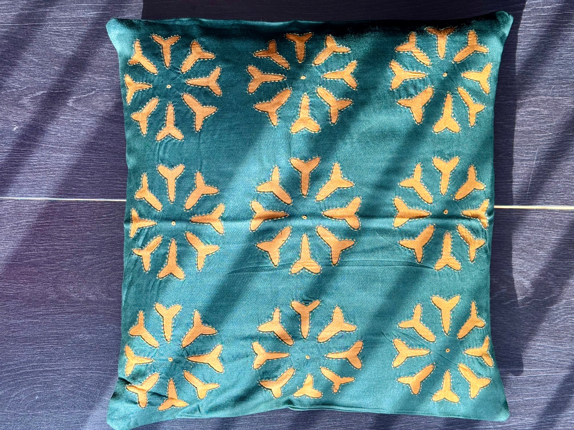 Teal pillow with yellow geometric pattern on a dark purple fabric background