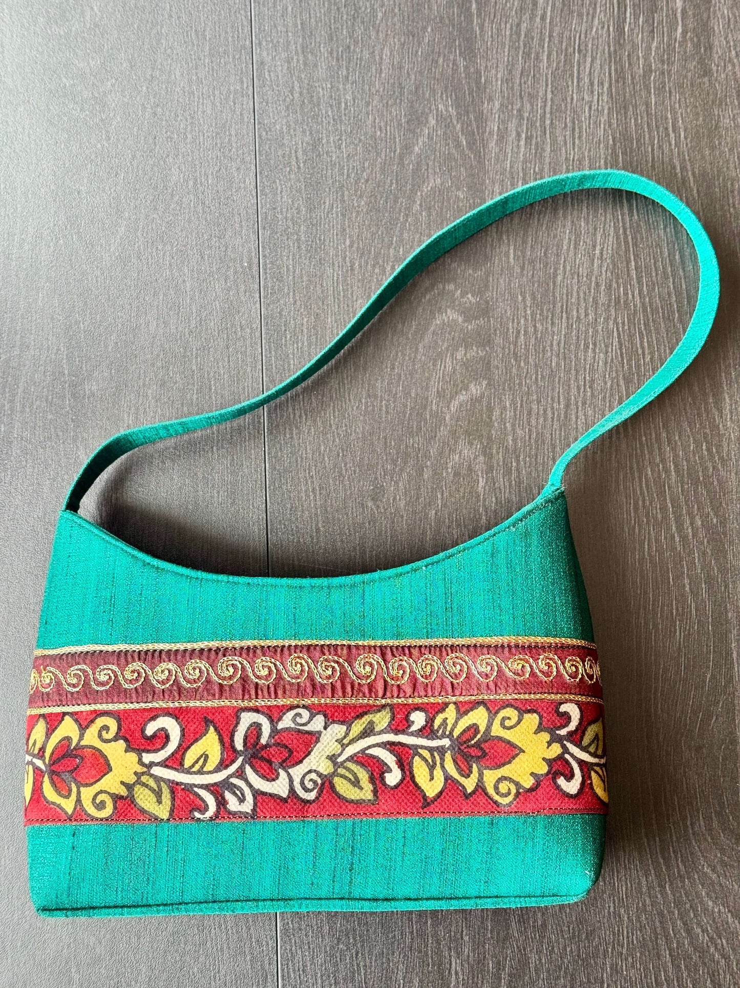 Turquoise handbag with decorative hand painted KalamkarI band on a wooden surface