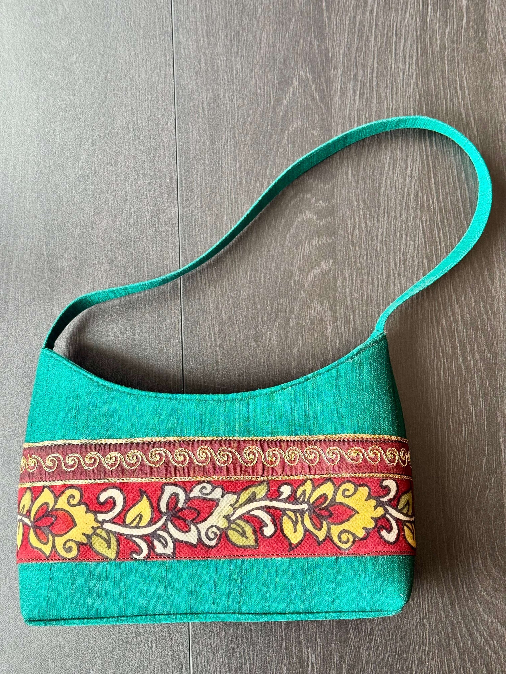 Turquoise handbag with decorative hand painted KalamkarI band on a wooden surface