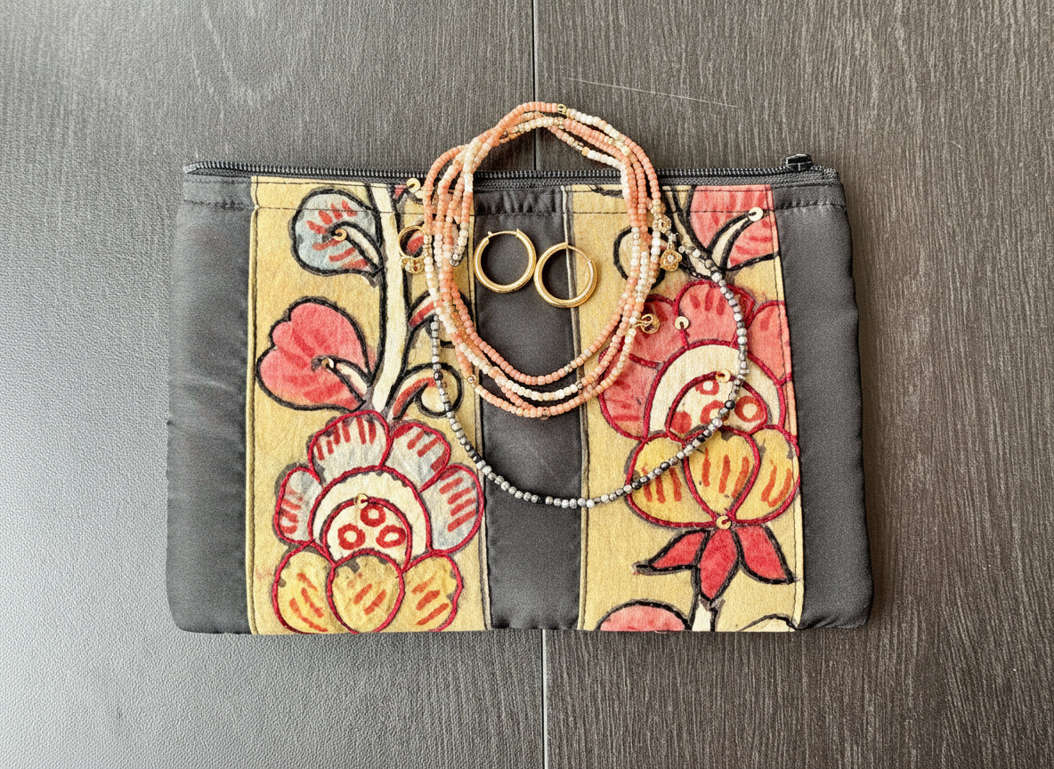 Close-up of a hand-painted makeup pouch with traditional Kalamkari art design featuring a bird and floral motifs in bright colors on a yellow background.