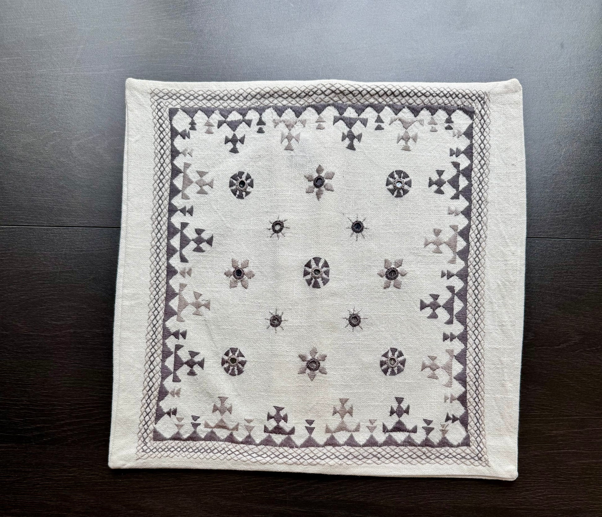 White Kutchi embroidery cushion cover with black patterns on a wooden surface