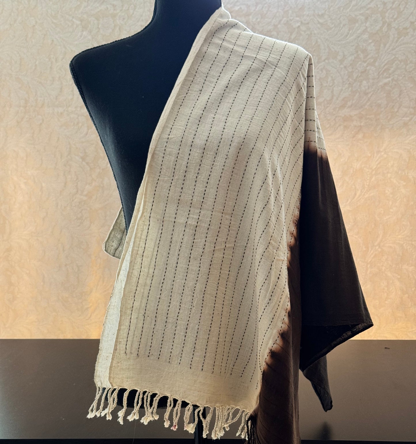 Beige cotton stole with black stripes draped over a black mannequin against a neutral wall.