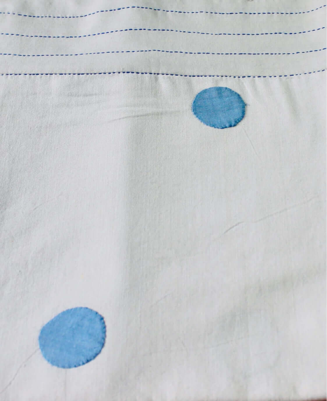 Close-up of white tablecloth with appliqué work blue circular patterns and stitching details.