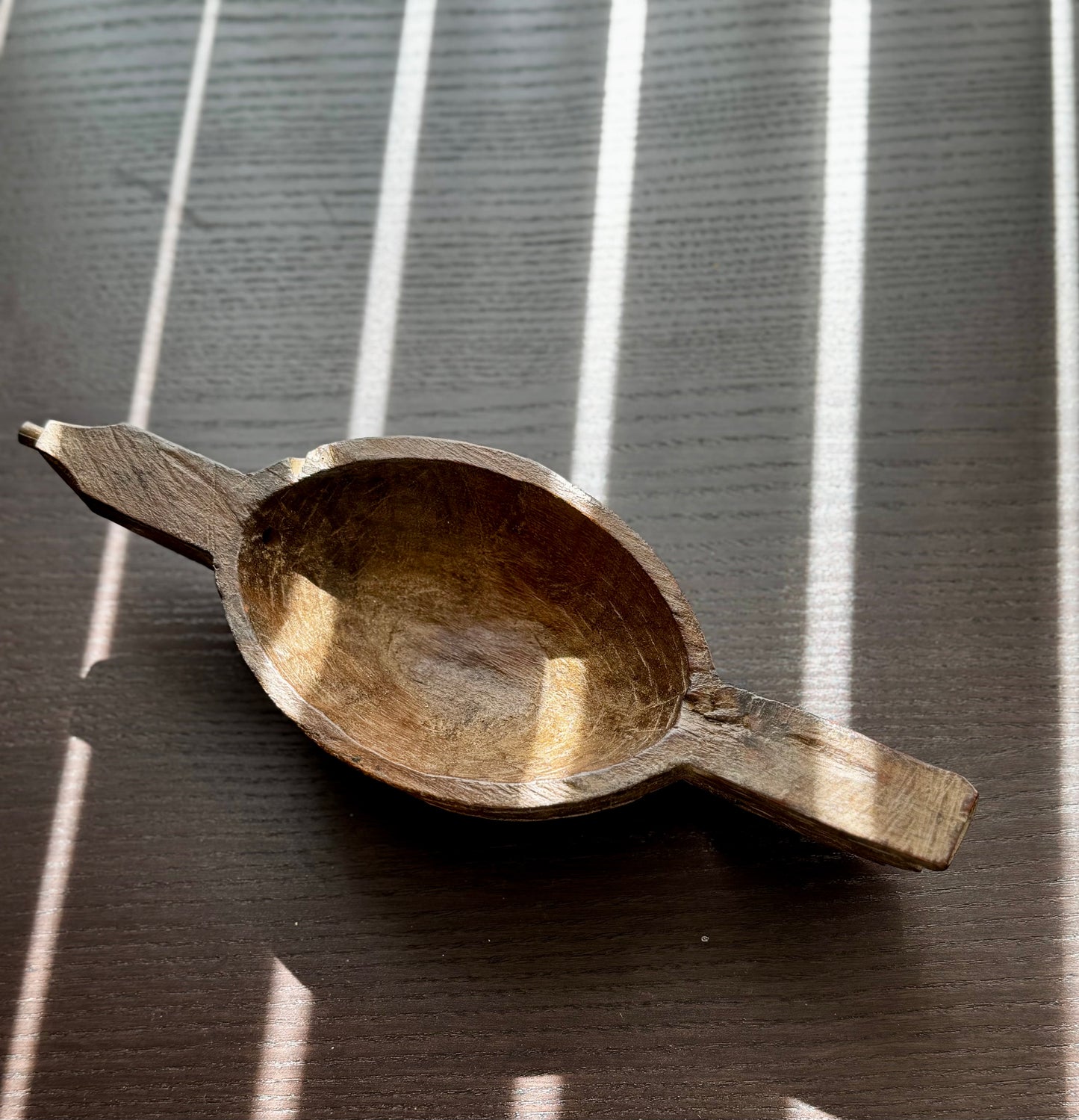 Wooden ladle like bowl on a dark surface with striped background